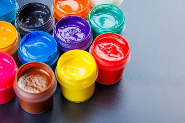 Close-up background of opened small gouache paint jars on black surface — Stockfoto