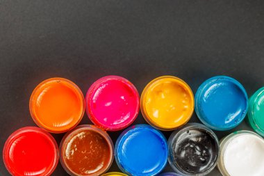 close-up background of opened small gouache paint jars on black surface