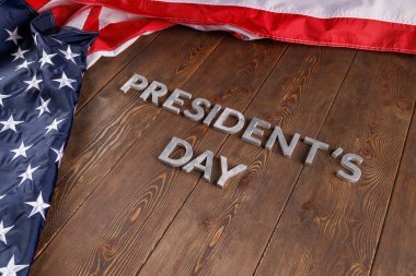 words presitdents day laid with silver letters on wooden surface near US flag