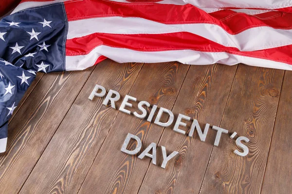 Words presitdents day laid with silver letters on wooden surface near US flag — Stock fotografie