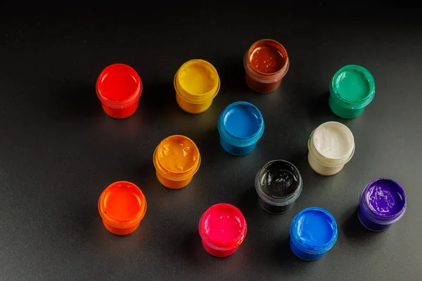 Close-up background of opened small gouache paint jars on black surface — Stockfoto