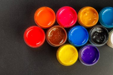 close-up background of opened small gouache paint jars on black surface