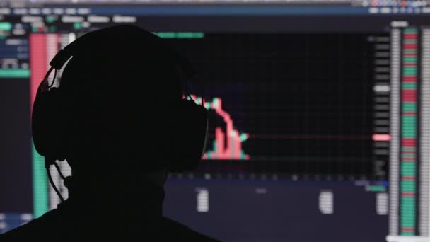 Unrecognizable man head in headphones in front of stock market trading chart with blurry japanese candlestick on black background — Vídeo de Stock