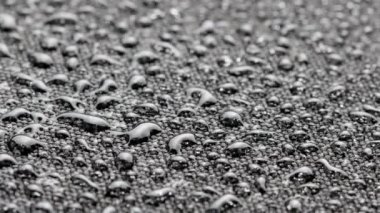 spinning closeup background of black hydrophobic fabric covered with water drops