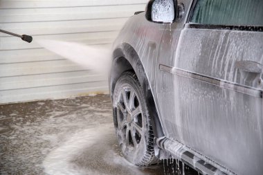 A process of flushing soap sud on silver car wheel with pressurised water stream at self-service indoor car wash station.
