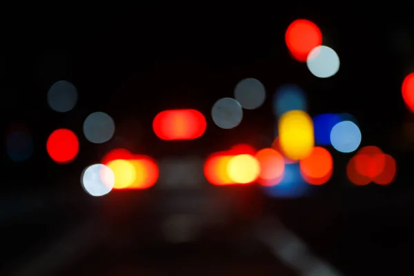 Defocused night street view from drivers perspective, with bokeh blur of street lights. Colorful night city life background.
