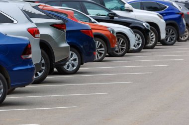 row of different color cars on asphalt parking lot at cloudy summer day with selective focus