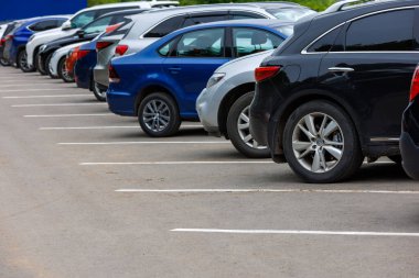 row of different color cars on asphalt parking lot at cloudy summer day with selective focus