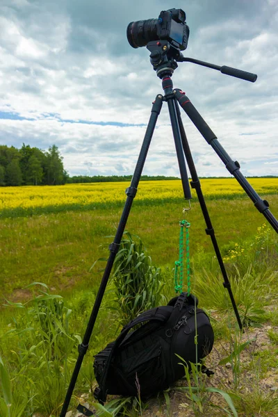 modern professional mirrorless camera on tripod shooting yellow field on tripod with black backpack underneath closeup with selective focus