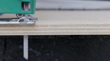 Sawdust flies off a metal blade as the jigsaw cuts into a sheet plywood workpiece. Carpenter cuts off the edge of a plywood plank. Jigsaw cuts into a piece of plywood. Side view.