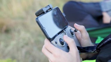 drone operator hands using remote control with sticks and cellphone as monitor at daylight on blurry wild grass background
