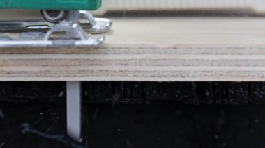 Sawdust flies off a metal blade as the jigsaw cuts into a sheet plywood workpiece. Carpenter cuts off the edge of a plywood plank. Jigsaw cuts into a piece of plywood. Side view.
