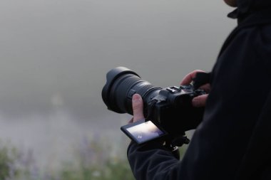 unrecognizable blurred caucasian photographer shooting misty outdoor scene with contemporary black digital camera on a tripod with flip screen