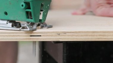Sawdust flies off a metal blade as the jigsaw cuts into a sheet plywood workpiece. Carpenter cuts off the edge of a plywood plank. Jigsaw cuts into a piece of plywood. Side view.