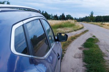 violet car on dry dirt road at summer evening with dry tall yellow grass and dark green forest in the background