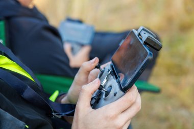 drone operator hands using remote control with sticks and cellphone as monitor at daylight on blurry wild grass background