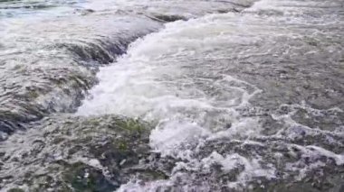 the flowing water of a summer river with a small rapid waterfall in slow motion at daylight.