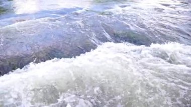 the flowing water of a summer river with a small rapid waterfall in slow motion at daylight.