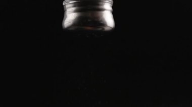 black pepper falling out from pepper-pot on black background in slow motion