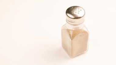 glass pepper-jar with stainless steel cap full of grounded black peppercorns spinning on white background, looped