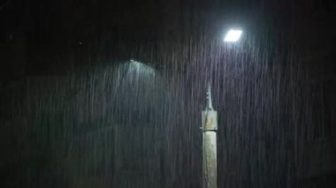 Double led panel lamppost under heavy rain at night. Midsize view of raindrops against a lamppost bright light. Static viewpoint. 180 degree shutter exposure with long raindrop tails