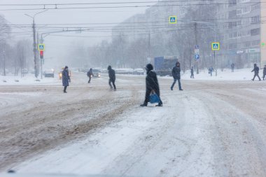 People in winter garment crossing winter street during heavy snowfall in daylight - December 25, 2021
