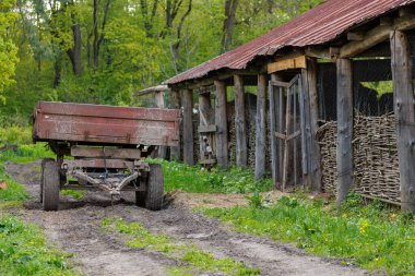an old agricultural trailer stands next to the stables in summer, close-up with selective focus.