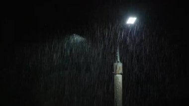 Double led panel lamppost under heavy rain at night. Midsize view of raindrops against a lamppost bright light. Static viewpoint.