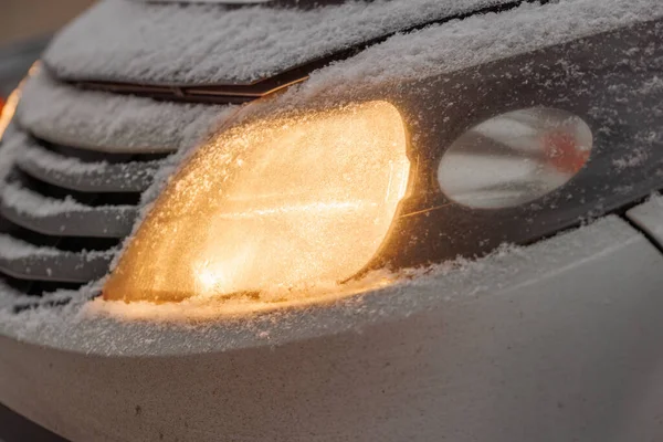 snow covered headlight of silver civiliian car at winter morning, close-up