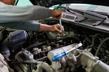 Hands of caucasian mechanic unscrewing diesel engine parts of modern SUV - sport utility vehicle with silver socket wrench. Closeup with selective focus,