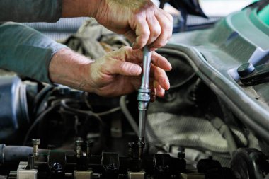 Hands of caucasian mechanic unscrewing diesel engine parts of modern SUV - sport utility vehicle with silver socket wrench. Closeup with selective focus,