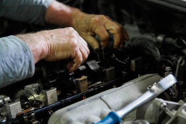 Hands of caucasian mechanic unscrewing diesel engine parts of modern SUV - sport utility vehicle with silver socket wrench. Closeup with selective focus,