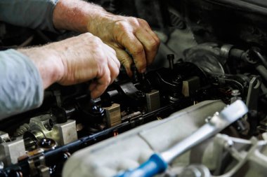 Hands of caucasian mechanic unscrewing diesel engine parts of modern SUV - sport utility vehicle with silver socket wrench. Closeup with selective focus,