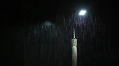 Double led panel lamppost under heavy rain at night. Midsize view of raindrops against a lamppost bright light. Static viewpoint. 180 degree shutter exposure with long raindrop tails