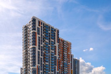 freshly built high rise apartment building on blue sky background with thin feathery clouds.