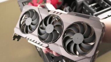 caucasian hand holding large and expensive air cooled computer graphic card with triple fan before installation into desktop personal computer
