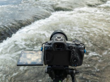 modern black digital mirrorless camera with flip-screen on tripod capturing streaming water, closeup view from back with selective focus