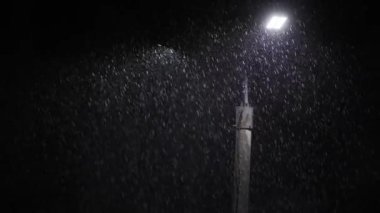 Double led panel lamppost under heavy rain at night. Midsize view of raindrops against a lamppost bright light. Static viewpoint. 180 degree shutter exposure with long raindrop tails