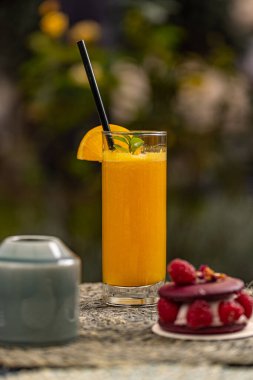 Kafe teras masasında portakal suyu ve bulanık bir pasta.