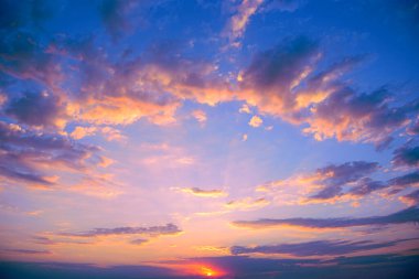 Fantastic pink sunset against bright blue sky with fluffy white clouds.