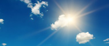 Blue sky with white clouds and bright sun with rays.