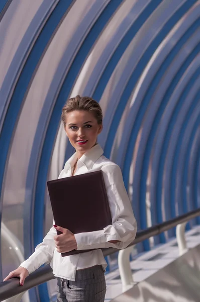 Young female businesswoman Carefully stands with a folder in his handr on the background a modern business center — Stock Photo, Image