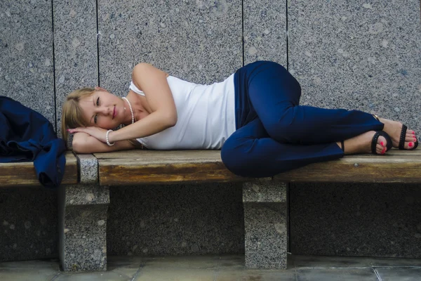 Mladá žena unavená podnikatel ležící na lavičce tvrdé denně na pozadí moderní obchodní centrum — Stock fotografie