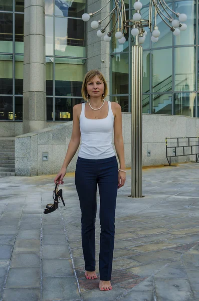 A young woman walks barefoot businessman after a hard day on the background of a modern business center — Stock Photo, Image