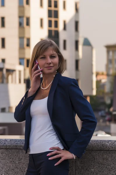 A young woman in a blue suit businessman talking on a cell phone on the background of a modern business center — Stock Photo, Image