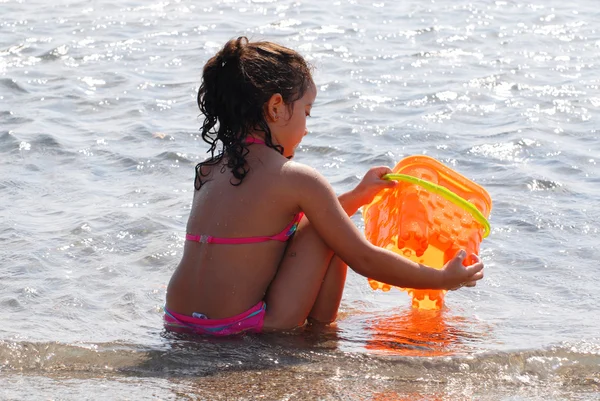 Small girl playing at a beach with a plastic bucket — Stock Photo, Image