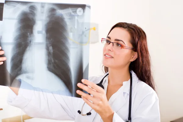 Молодая женщина-врач смотрит на рентген груди пациента — стоковое фото