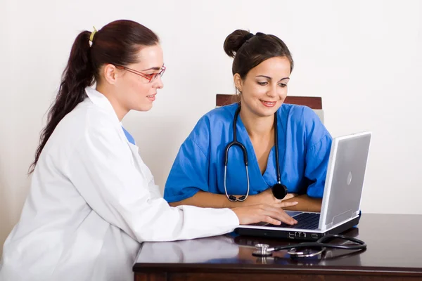 Doctora y enfermera usando computadora portátil en la oficina —  Fotos de Stock