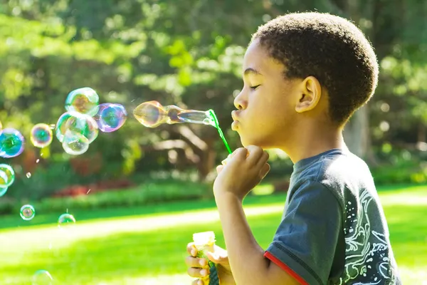 African boy blowing bubbles at the park — Stock Photo, Image