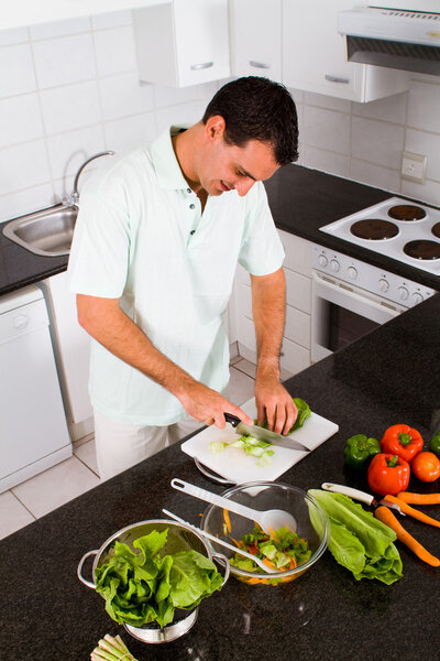 молодой человек режет овощи на кухне
